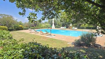 Una piscina circondata dal verde, con lettini e cielo sereno.