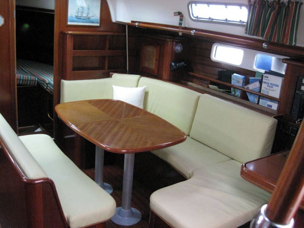 A compact interior with a wooden table and cushioned seating, a small window, and a shelf with items.