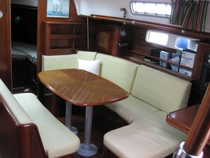 A compact interior with a wooden table and cushioned seating, a small window, and a shelf with items. - Sun-kissed Sailing Adventure in the Ionian Islands (Preveza)