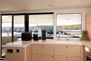 Een moderne keuken met uitzicht op boten en een steiger, houten kastjes en een koffiezetapparaat.