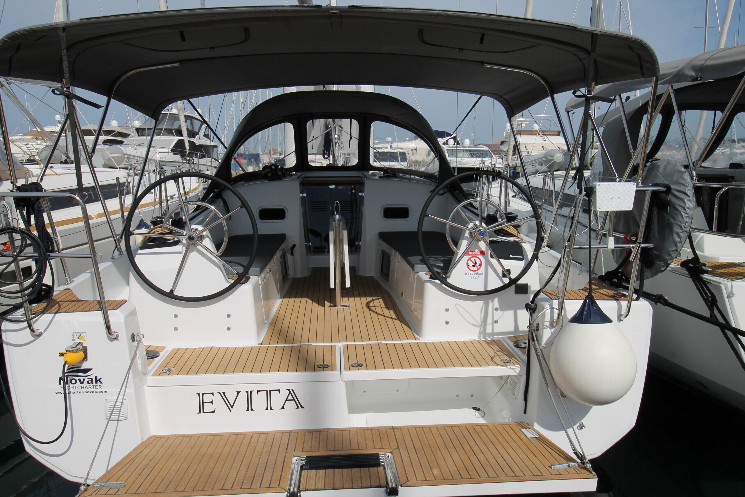 Un pont de bateau avec une roue de barre, le nom « EVITA » écrit sur le côté et le logo « Novak Charter ».