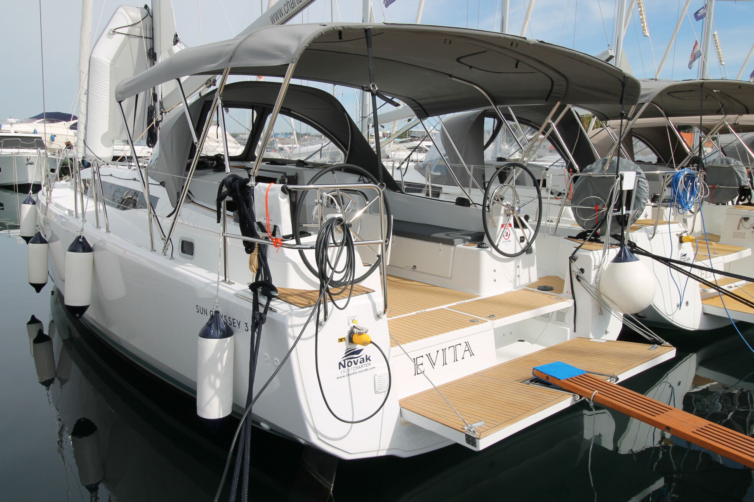 A yacht named 'EVITA' docked at a marina with other boats, featuring a wooden deck, a steering wheel, and a logo for 'Novak'.