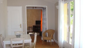 Um quarto com uma mesa de jantar, cadeiras, televisão e uma cadeira de vime.