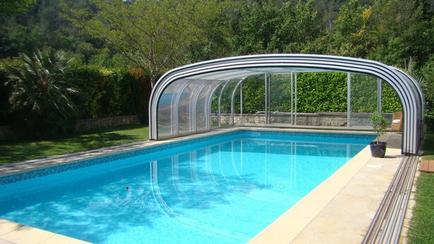 Piscina com superfície de água azul e límpida, rodeada por área coberta com teto curvo.