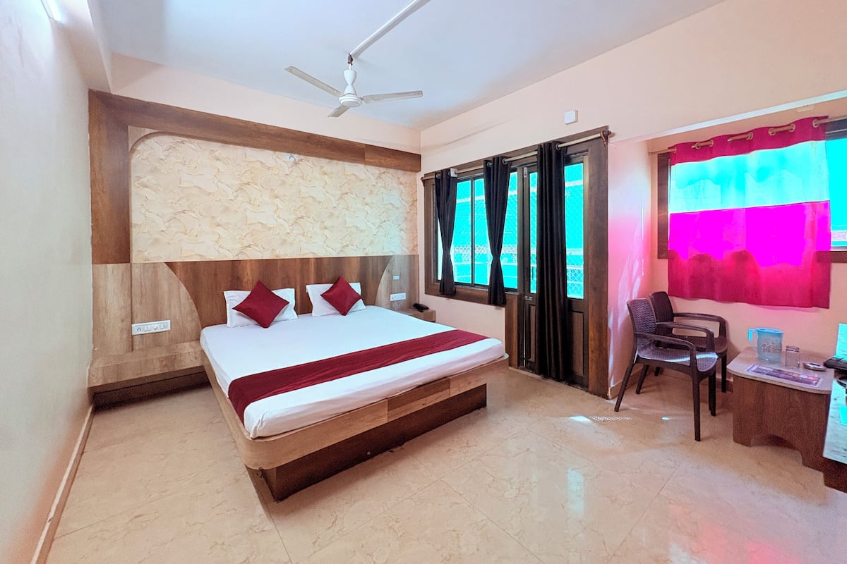 Habitación de hotel con cama, escritorio, silla, ventilador de techo y ventana con cortinas.