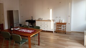 Una cucina moderna con frigorifero, lavello e pensili in legno. Si vede un tavolo da pranzo con sedie e una lampada sopra.