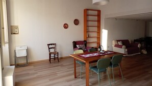 Un'area pranzo con tavolo in legno, quattro sedie, una scala e un divano con cuscini.