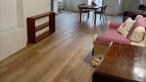 Un'ampia zona giorno con pavimento in legno, un tavolo da pranzo con sedie, un divano e una panca.