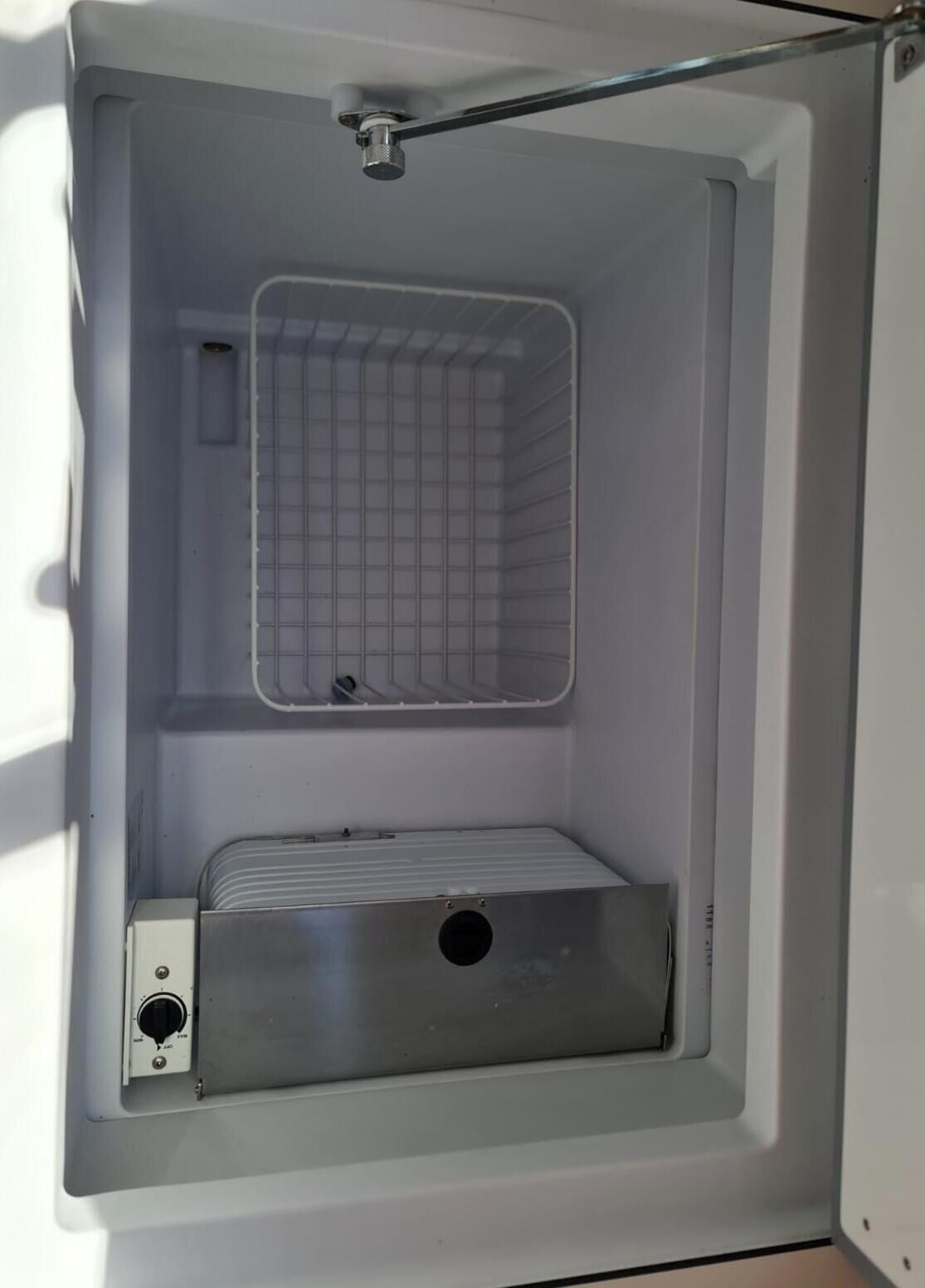A compact, white room with a metal grid shelf, a control panel, and a metal box.