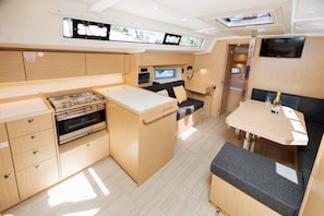 A compact kitchen with a stove, oven, and a small dining area with a table and bench. - Sun-Kissed Sailing Adventure in Zadar, Croatia (Zadar)