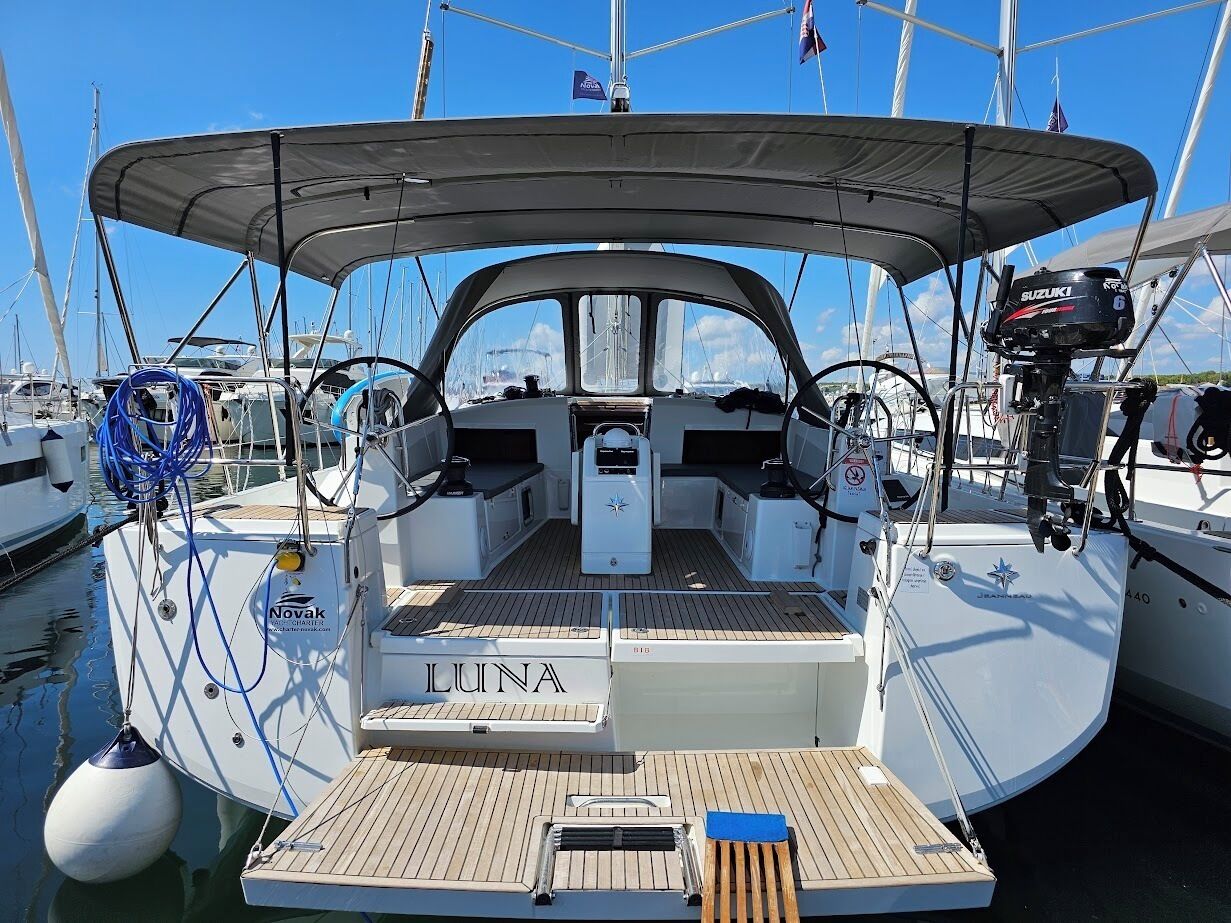 Un velero amarrado en un puerto deportivo con cubierta protegida, un motor fueraborda Suzuki y el nombre 'LUNA' en la proa.