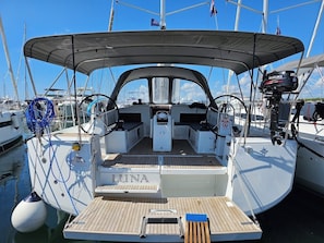 Eine Segelyacht liegt in einer Marina festgemacht, mit einer überdachten Deck und einem Suzuki Außenmotor. Auf dem Bug ist der Name 'LUNA' zu sehen.
