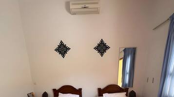A room with two wooden beds, a wall-mounted air conditioner, decorative wall art, a mirror, and a window with curtains.