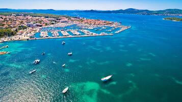 An aerial view of a coastal town with a marina, boats, and a clear blue sea.