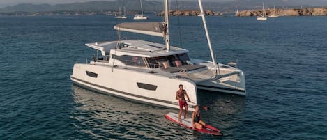 Un yacht doté d’un pont couvert et une personne debout sur une planche de paddle.
