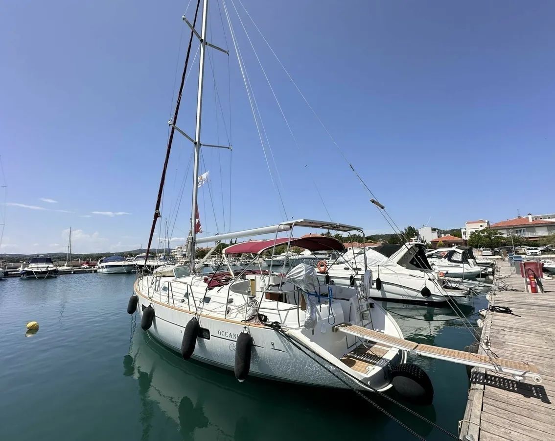 Un port de plaisance où sont amarrés plusieurs voiliers, une jetée en bois et un ciel bleu azur.