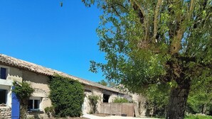 Un edificio rústico con fachada de piedra, un árbol en primer plano y un cielo azul despejado.