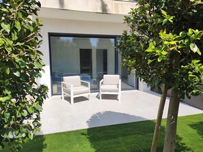 A modern outdoor seating area with two white chairs and a glass door leading to an interior space. - Golf course villa sleeping 8–10 with ocean views, 8 minutes from the beaches (Bonmont Terres Noves)