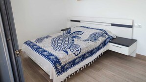 Ein Schlafzimmer mit einem Bett, einem Nachttisch, einem Bild einer Strandansicht und einer Tür.