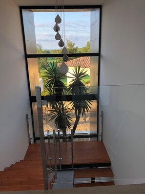 Una escalera moderna con barandillas de cristal y vistas a un jardín ajardinado.