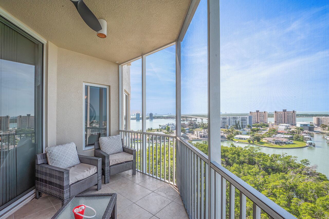 A balcony with wicker furniture, a glass door, and a view of a cityscape and river.