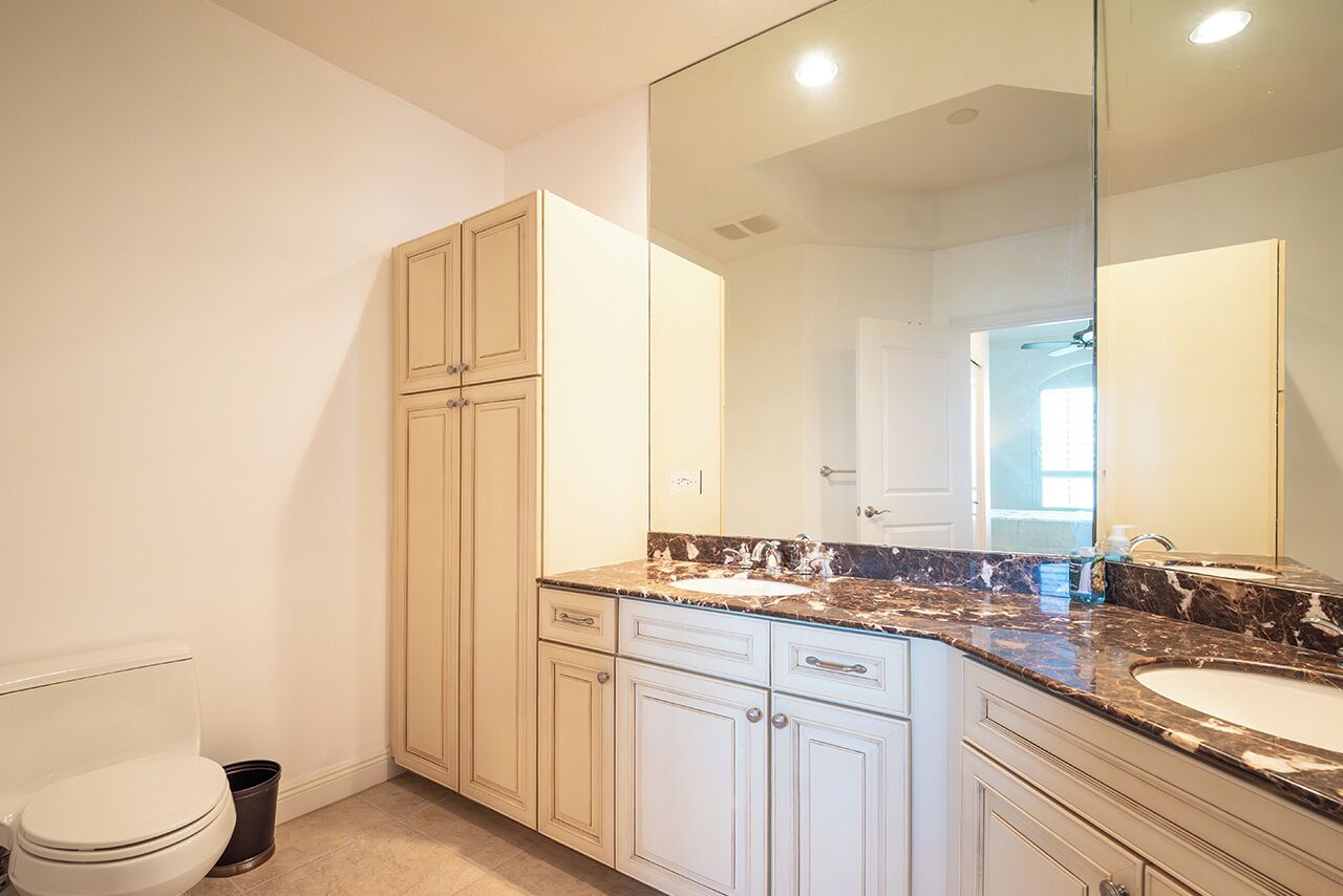 A bathroom with a toilet, a sink, a mirror, and cabinets.
