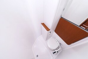 Een compacte, moderne badkamer met een wit toilet, een houten wastafelmeubel en een witte wasbak.