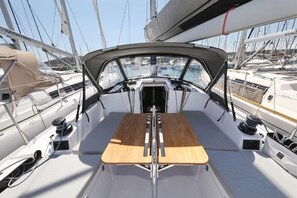 Het dek van een zeilboot met een centrale tafel, lieren en een mast.