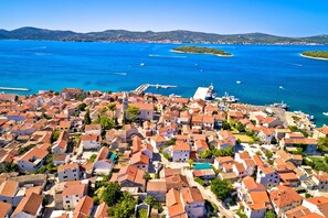A coastal town with red-roofed buildings, a marina, and clear blue waters.