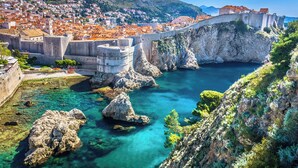 A coastal town with a historic stone bridge, clear turquoise waters, and a mountainous backdrop.