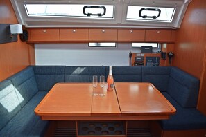 Uma cabana compacta com uma mesa central, duas áreas de estar acolchoadas em azul e uma pequena cozinha, além de claraboias.