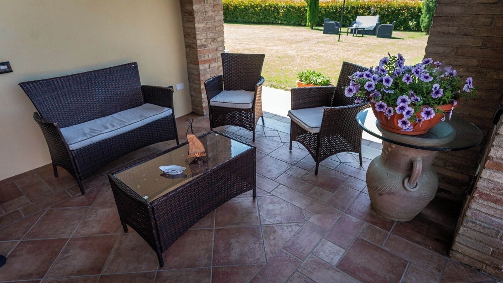 Una zona patio con mobili in vimini, un tavolo con piano in vetro e una pianta in vaso.