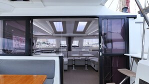 Jachtinnenraum mit Essbereich, einer Sitzecke mit Tisch und Blick auf den Hafen durch große Fenster.