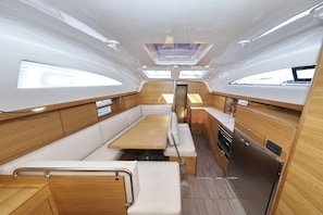 A yacht interior with a central seating area, wooden cabinetry, and a galley with a refrigerator. - Sun-Kissed Sailing Adventure in Zadar, Croatia (Biograd na moru)