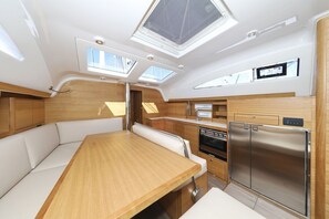 A compact galley with a wooden table, white cushioned seating, a stainless steel refrigerator, and a small oven. - Sun-Kissed Sailing Adventure in Zadar, Croatia (Biograd na moru)