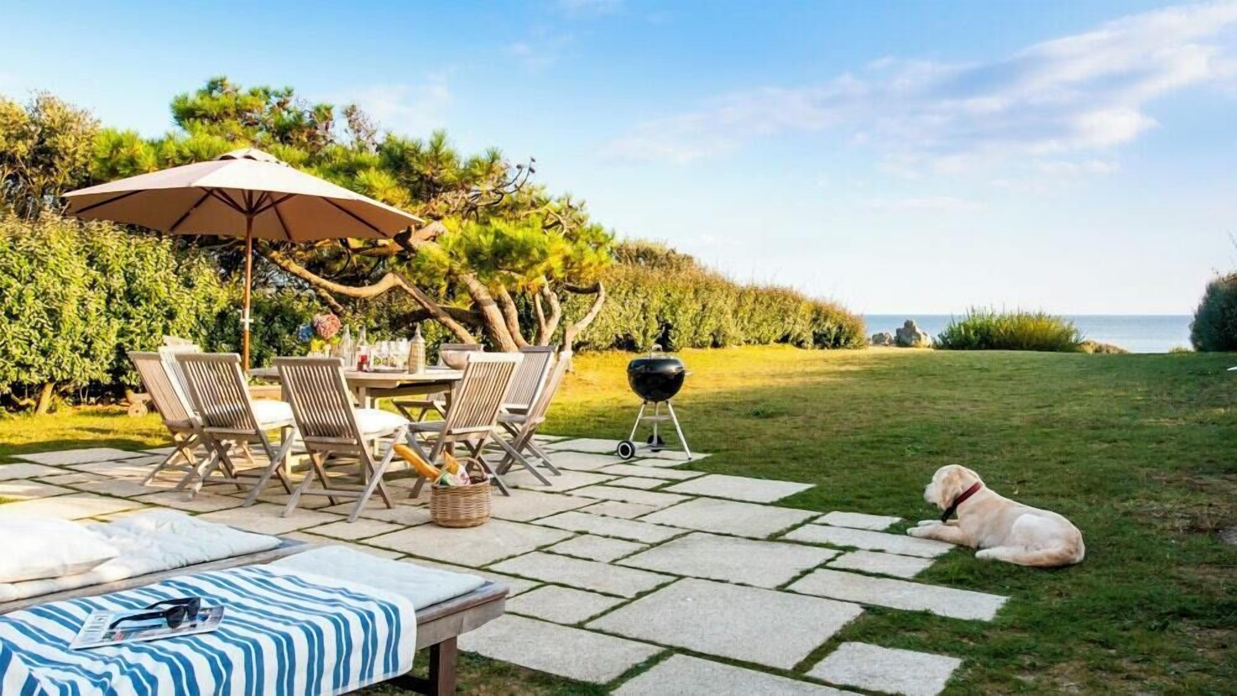 Eine Terrasse im Freien mit Tisch, Stühlen, einem Grill und einem Hund.