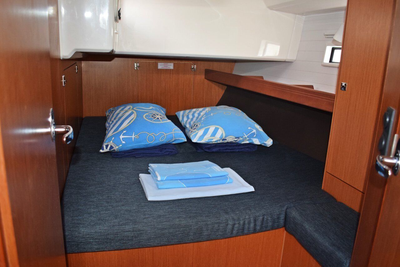 Een klein bed met twee kussens, een opgevouwen deken en een hoofdbord in een blokhut met houten wanden en een klein raam.