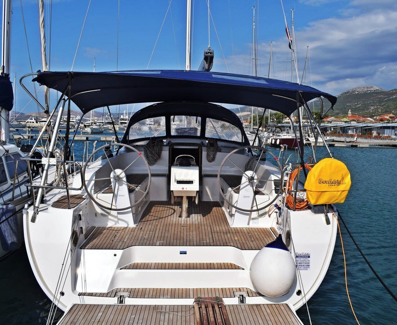 Een zeilboot afgemeerd in een jachthaven, met een overdekt dek, stuurwiel en reddingsboei.