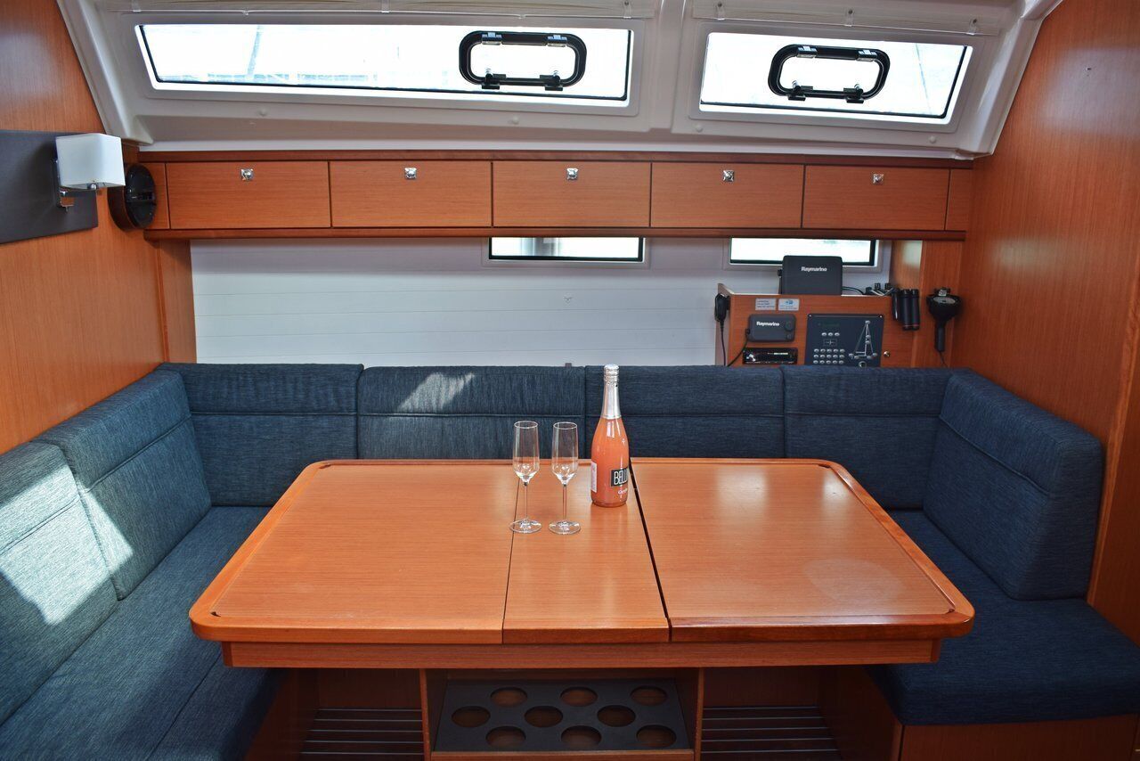 A compact cabin with a central table, two blue cushioned seating areas, a small kitchenette, and skylights.