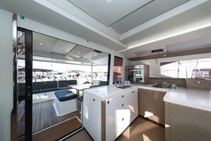 A modern kitchen with a central island, a dining area with a bench, and a view of the marina. - Sun-kissed Sailing Adventure in Split-Dalmatia, Croatia (Trogir)