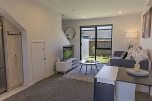 A modern living room with a flat-screen TV, a sofa, a small round table, and a sliding glass door leading to a backyard.