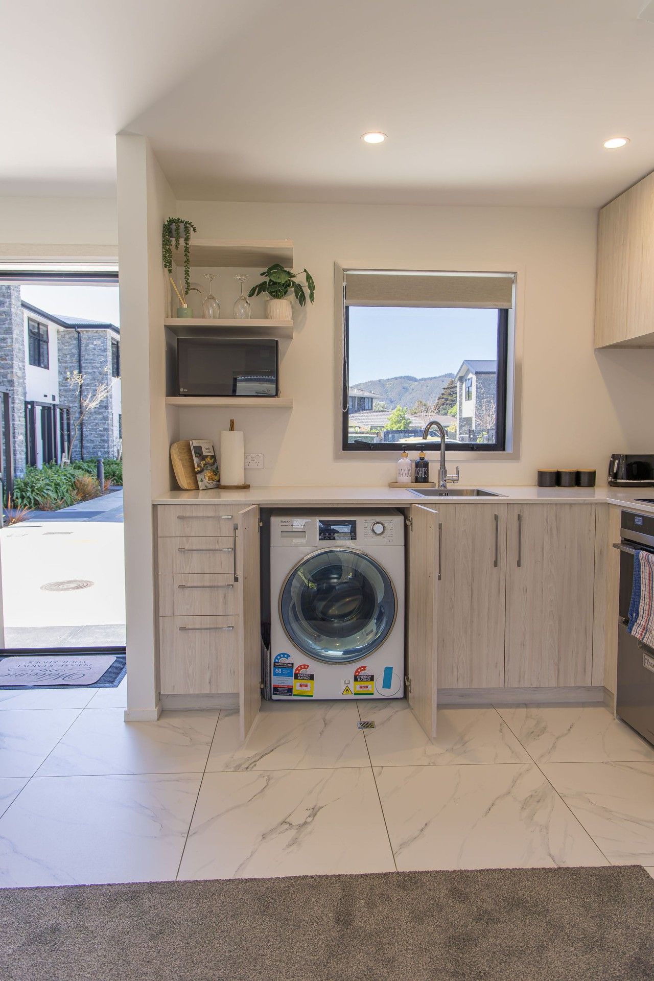 Une cuisine moderne équipée d’un lave-linge intégré, d’une fenêtre avec vue et d’un évier.