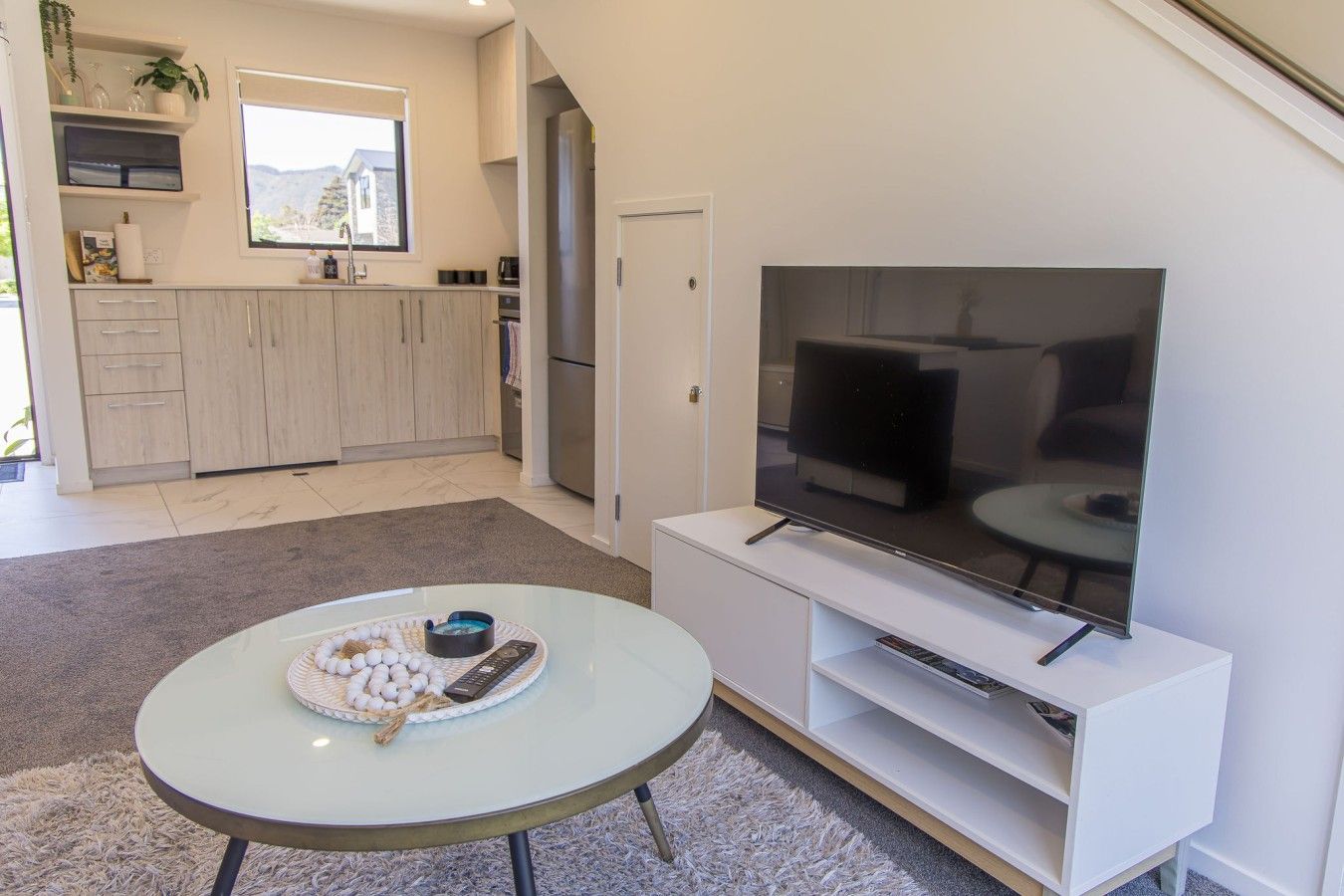 A modern kitchen with a large TV, a dining area with a round table, and a view of the outdoors.