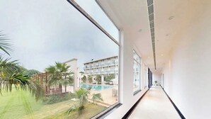 A corridor with large windows, a pool, and a building with balconies. - Sunday Resort & Spa Manesar Gurugram (Taoru)
