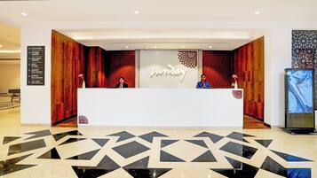 A hotel reception desk with a 'Sunday' sign, a directional sign for the elevator and fitness center, and a patterned floor.