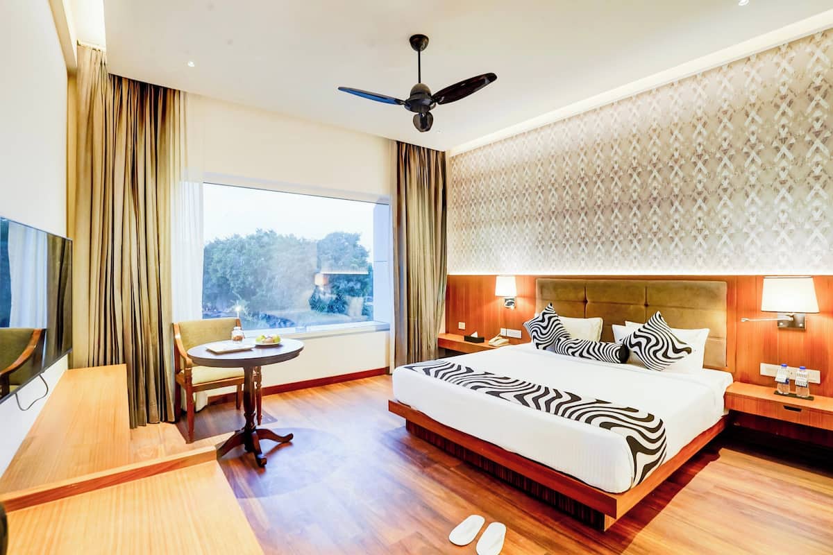 Una habitación de hotel con cama, escritorio, silla, ventana y ventilador de techo.