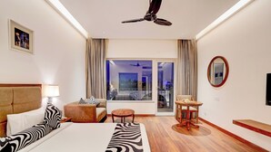 A hotel room with a bed, a ceiling fan, a window with curtains, a small table, and a TV. - Sunday Resort & Spa Manesar Gurugram (Taoru)