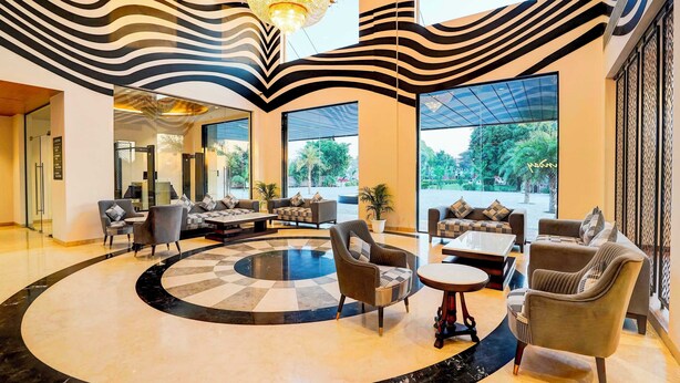 A lobby with a circular seating area, large windows, and a chandelier. - Sunday Resort & Spa Manesar Gurugram (Taoru)
