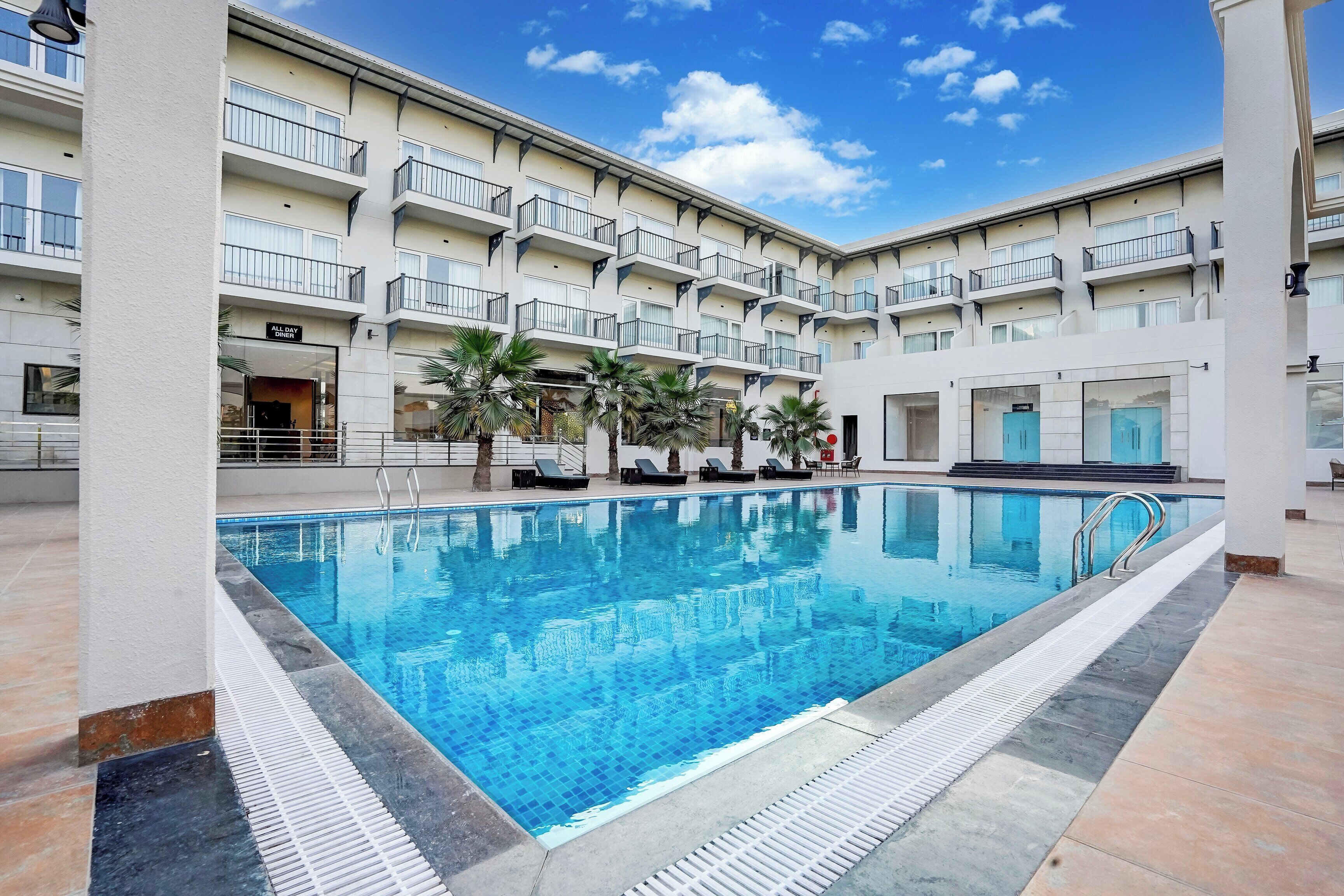 A hotel with a swimming pool, multiple balconies, and palm trees.