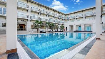 A hotel with a swimming pool, multiple balconies, and palm trees.